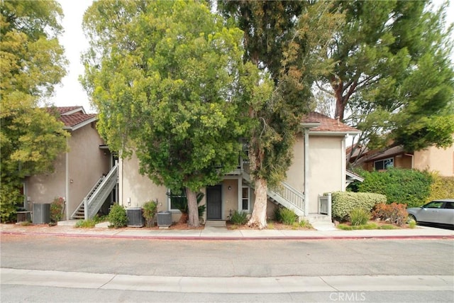 view of property hidden behind natural elements with stairs, central air condition unit, and stucco siding