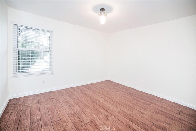 spare room with baseboards and wood finished floors