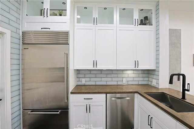 kitchen featuring dark countertops, white cabinets, appliances with stainless steel finishes, and a sink