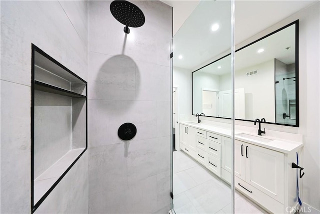 full bathroom featuring a tile shower, visible vents, double vanity, and a sink