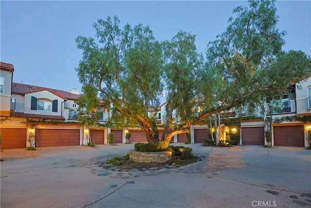 view of property with a tile roof, an attached garage, driveway, and stucco siding