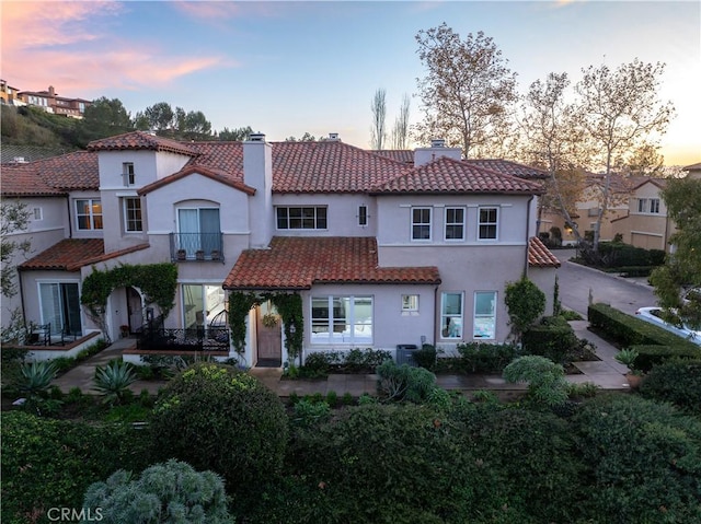 mediterranean / spanish-style house featuring stucco siding, a balcony, a chimney, and a tile roof