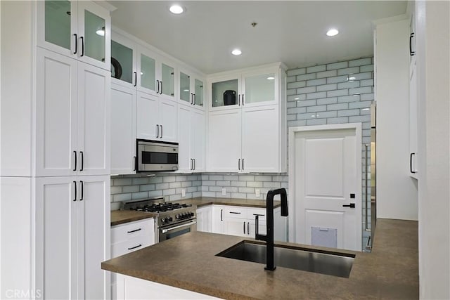 kitchen with dark countertops, tasteful backsplash, appliances with stainless steel finishes, white cabinetry, and a sink