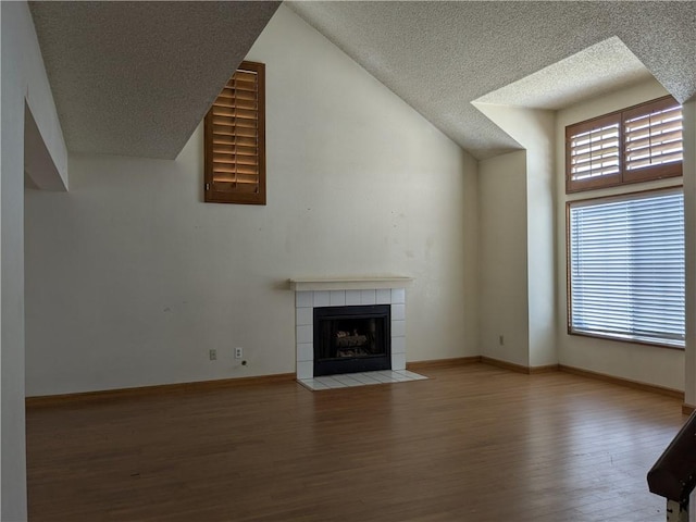 unfurnished living room with a tiled fireplace, a textured ceiling, baseboards, and wood finished floors