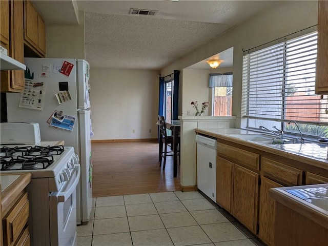 kitchen with visible vents, brown cabinetry, light tile patterned flooring, white appliances, and a sink