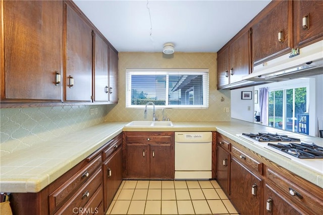 kitchen featuring decorative backsplash, white appliances, under cabinet range hood, and a sink