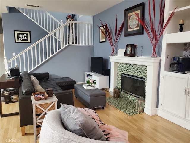 living room with visible vents, wood finished floors, stairs, and a tile fireplace