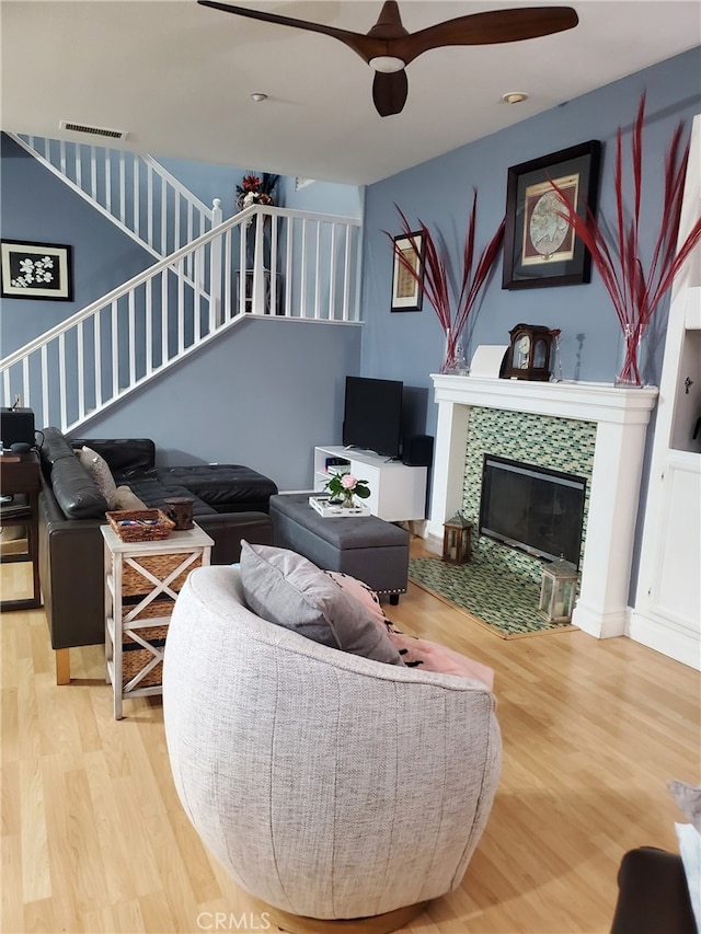 living room with visible vents, a ceiling fan, wood finished floors, a fireplace, and stairs