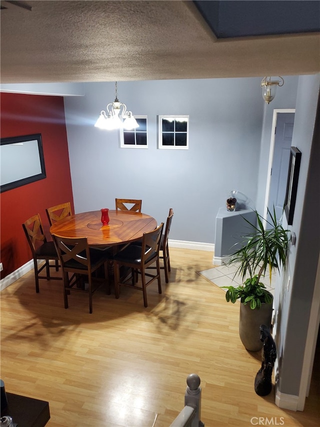 dining space with light wood-type flooring, baseboards, a notable chandelier, and a textured ceiling