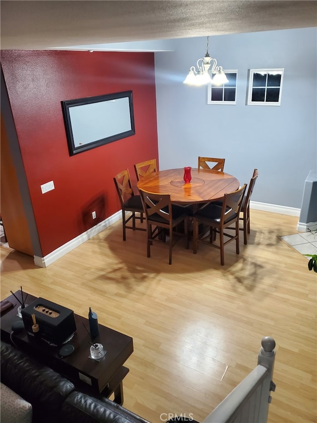 dining space with a textured ceiling, baseboards, light wood-type flooring, and a chandelier