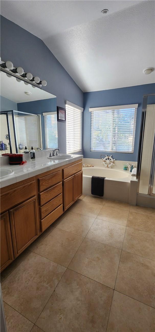 full bath with double vanity, a sink, vaulted ceiling, a garden tub, and tile patterned floors