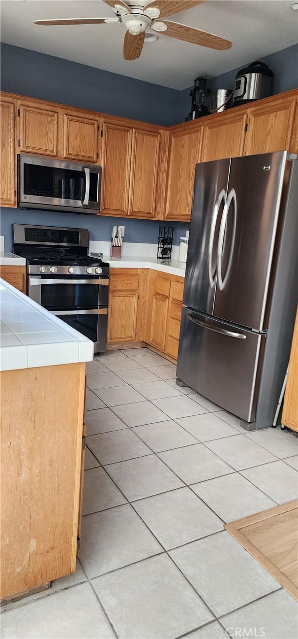 kitchen with a ceiling fan, light tile patterned flooring, light countertops, appliances with stainless steel finishes, and brown cabinets