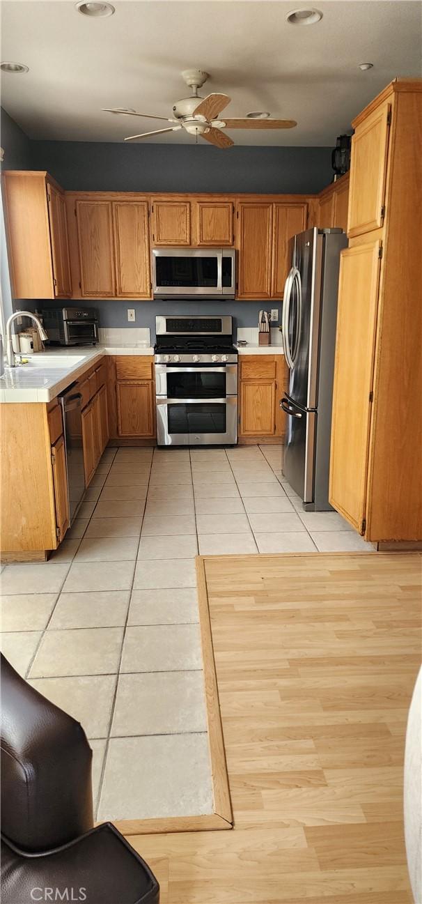 kitchen featuring light tile patterned floors, a sink, ceiling fan, light countertops, and stainless steel appliances