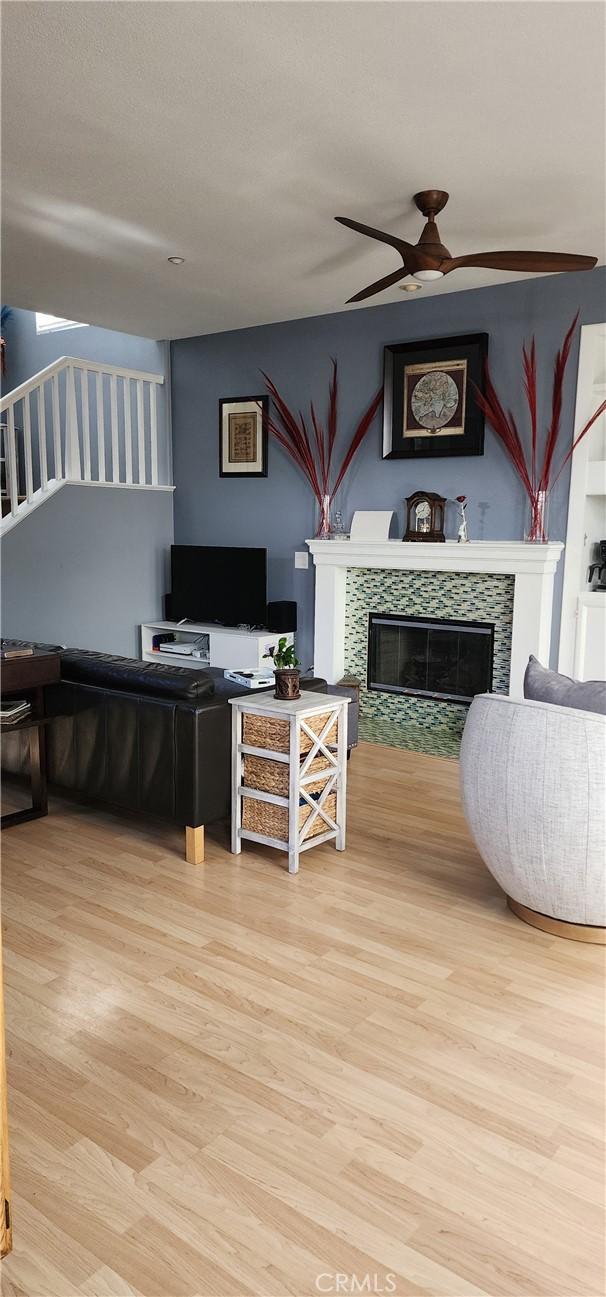 living room featuring a fireplace, stairs, wood finished floors, and ceiling fan