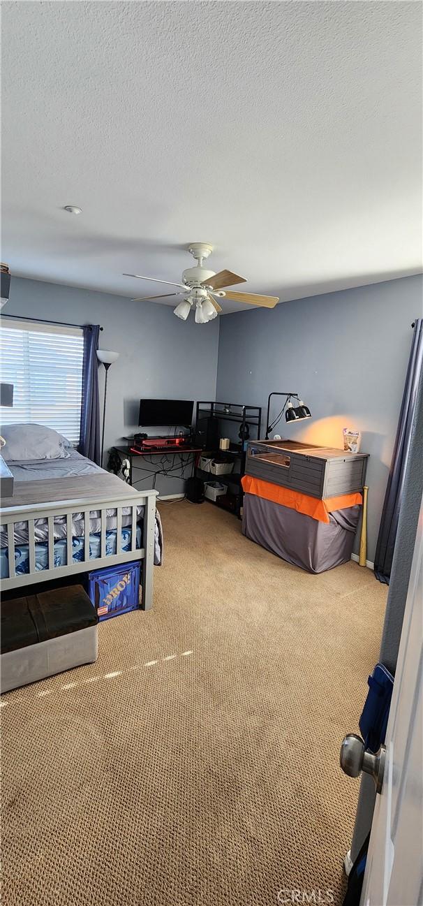 carpeted bedroom with a ceiling fan and a textured ceiling