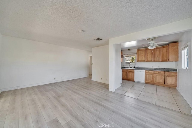 kitchen featuring brown cabinetry, visible vents, light wood-style flooring, white dishwasher, and a sink