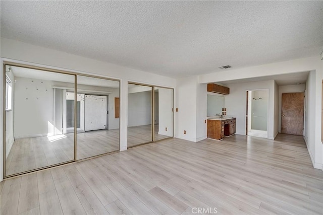 unfurnished bedroom with visible vents, multiple closets, a textured ceiling, and light wood-style flooring