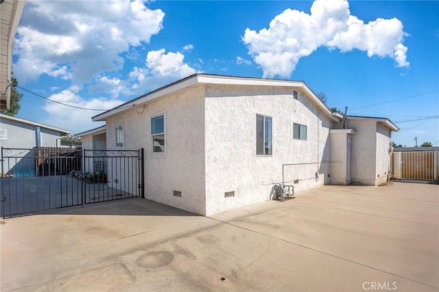 view of side of home with crawl space, fence, stucco siding, and a gate