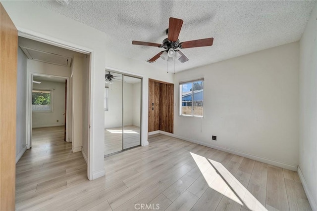 unfurnished bedroom featuring multiple windows, attic access, light wood-type flooring, and multiple closets