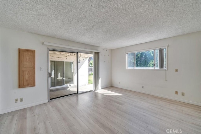 spare room featuring baseboards, light wood finished floors, and a textured ceiling