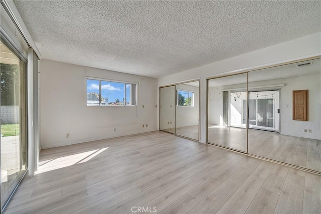 unfurnished bedroom with visible vents, light wood-type flooring, two closets, and a textured ceiling