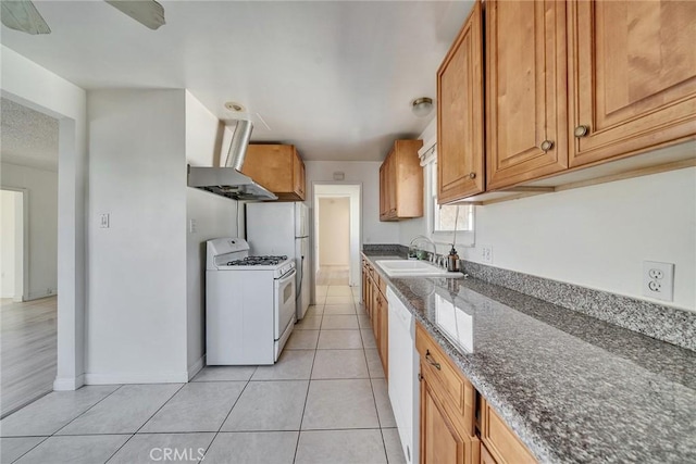 kitchen with white appliances, dark stone countertops, range hood, light tile patterned floors, and a sink