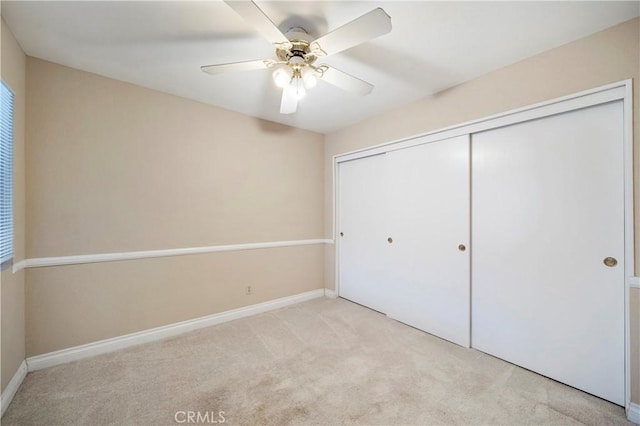 unfurnished bedroom featuring light carpet, ceiling fan, baseboards, and a closet