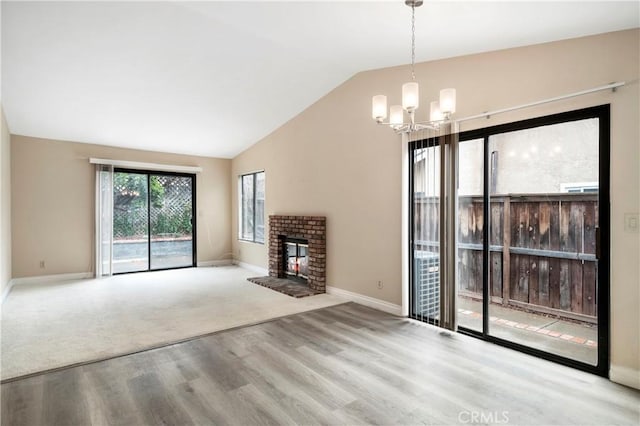 unfurnished living room featuring a brick fireplace, baseboards, lofted ceiling, wood finished floors, and a notable chandelier