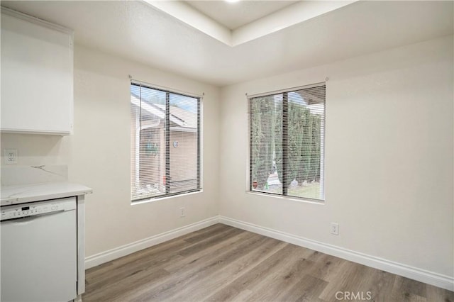 unfurnished dining area featuring a raised ceiling, light wood-style floors, and baseboards