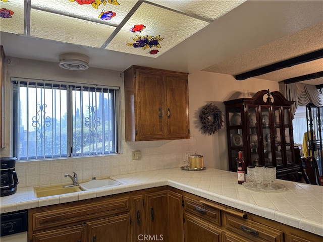 kitchen featuring brown cabinetry, a sink, light countertops, dishwasher, and backsplash