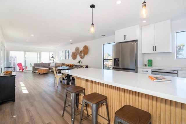 kitchen featuring stainless steel appliances, hanging light fixtures, light countertops, white cabinets, and light wood-style floors