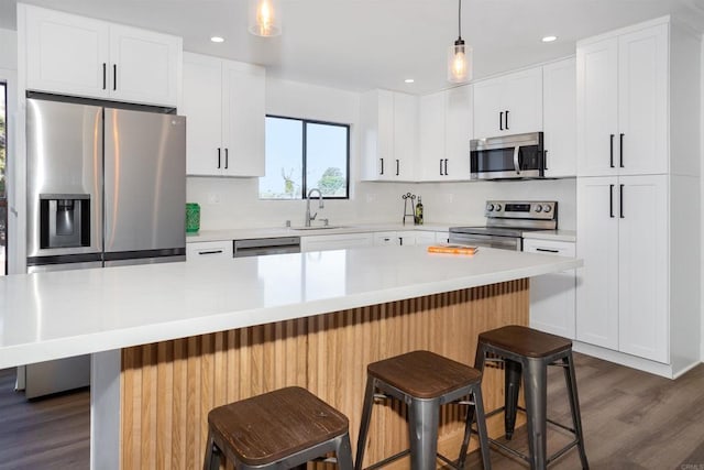 kitchen with a sink, backsplash, appliances with stainless steel finishes, white cabinets, and dark wood-style flooring