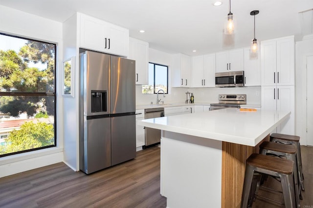 kitchen featuring dark wood-type flooring, a kitchen bar, light countertops, appliances with stainless steel finishes, and a sink