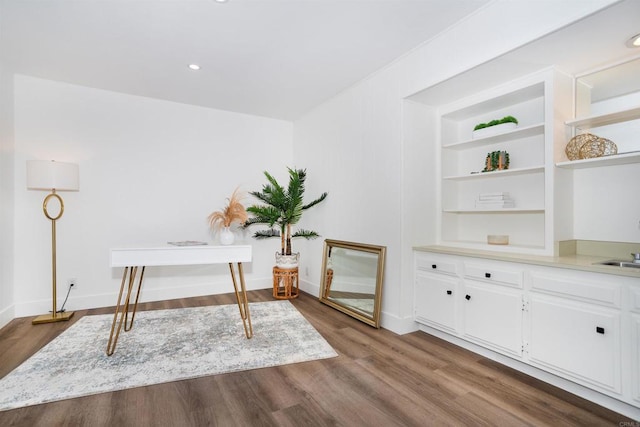 unfurnished office featuring built in shelves, a sink, dark wood finished floors, recessed lighting, and baseboards