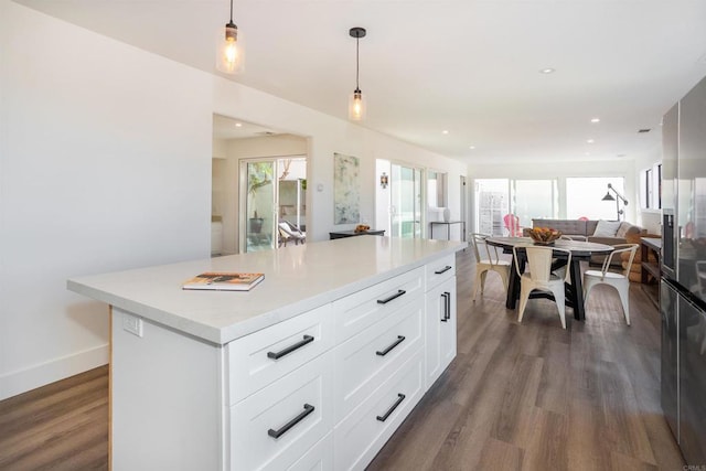 kitchen featuring a kitchen island, open floor plan, pendant lighting, light countertops, and dark wood-style flooring