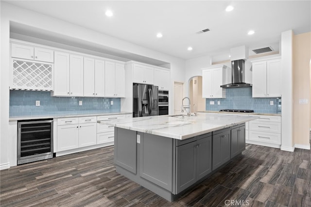 kitchen featuring gray cabinetry, wine cooler, appliances with stainless steel finishes, arched walkways, and wall chimney exhaust hood