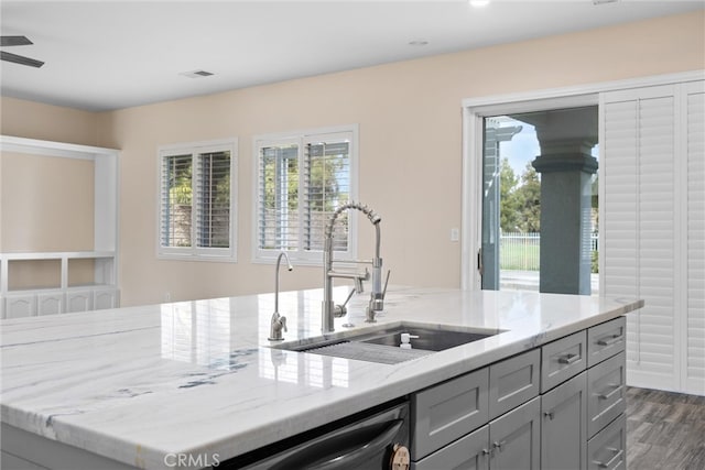 kitchen with dark wood-type flooring, gray cabinetry, a sink, dishwashing machine, and light stone countertops