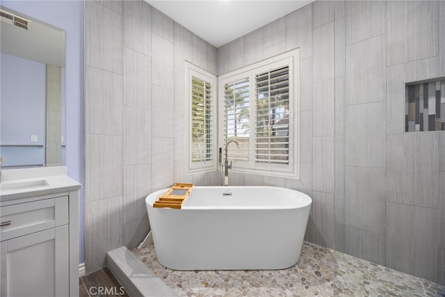 bathroom with visible vents, tile walls, vanity, and a freestanding tub