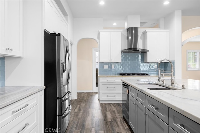 kitchen with stainless steel appliances, arched walkways, white cabinetry, wall chimney exhaust hood, and a sink