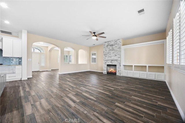 unfurnished living room featuring a tiled fireplace, dark wood-style floors, baseboards, and ceiling fan