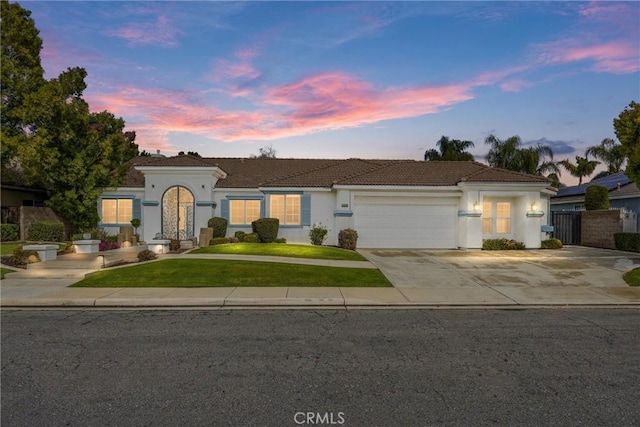 view of front of property featuring a tiled roof, stucco siding, a lawn, a garage, and driveway