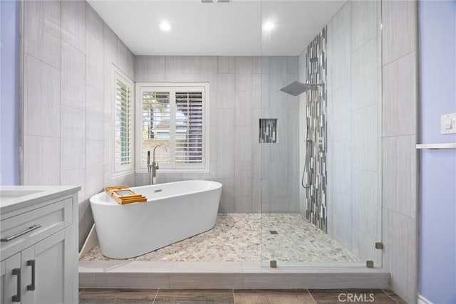 full bath featuring tiled shower, a freestanding bath, tile walls, and vanity