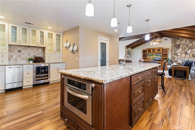 kitchen with open floor plan, light wood-style floors, appliances with stainless steel finishes, and beverage cooler