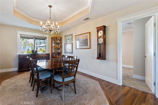 dining room with a raised ceiling, wood finished floors, visible vents, and a chandelier