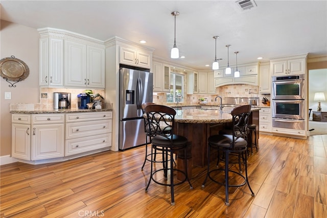 kitchen featuring a warming drawer, visible vents, light wood-style flooring, a kitchen breakfast bar, and appliances with stainless steel finishes