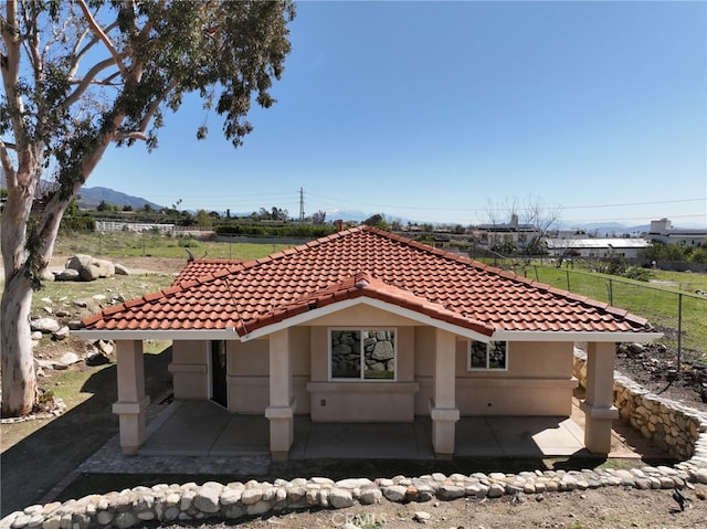 exterior space featuring a tile roof, a patio area, fence, and stucco siding