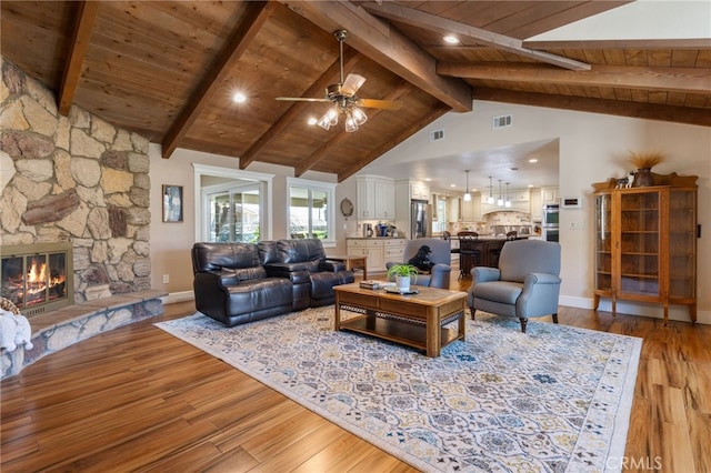 living area with visible vents, vaulted ceiling with beams, light wood-type flooring, a stone fireplace, and wooden ceiling