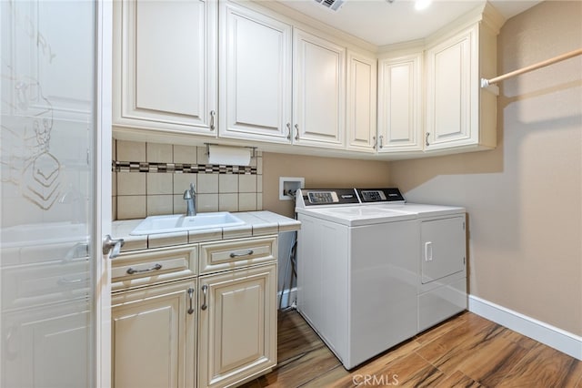 washroom featuring washer and clothes dryer, cabinet space, light wood-style floors, and a sink