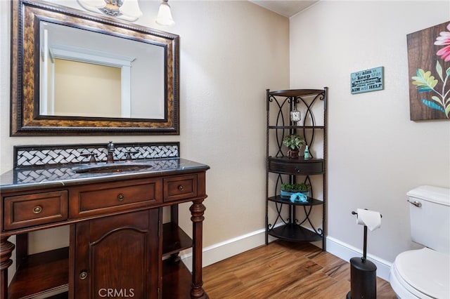 half bath featuring baseboards, toilet, wood finished floors, and vanity