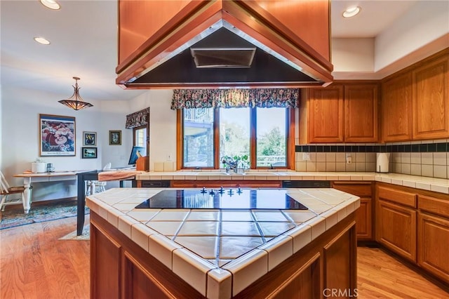 kitchen featuring premium range hood, brown cabinetry, tile counters, and light wood finished floors